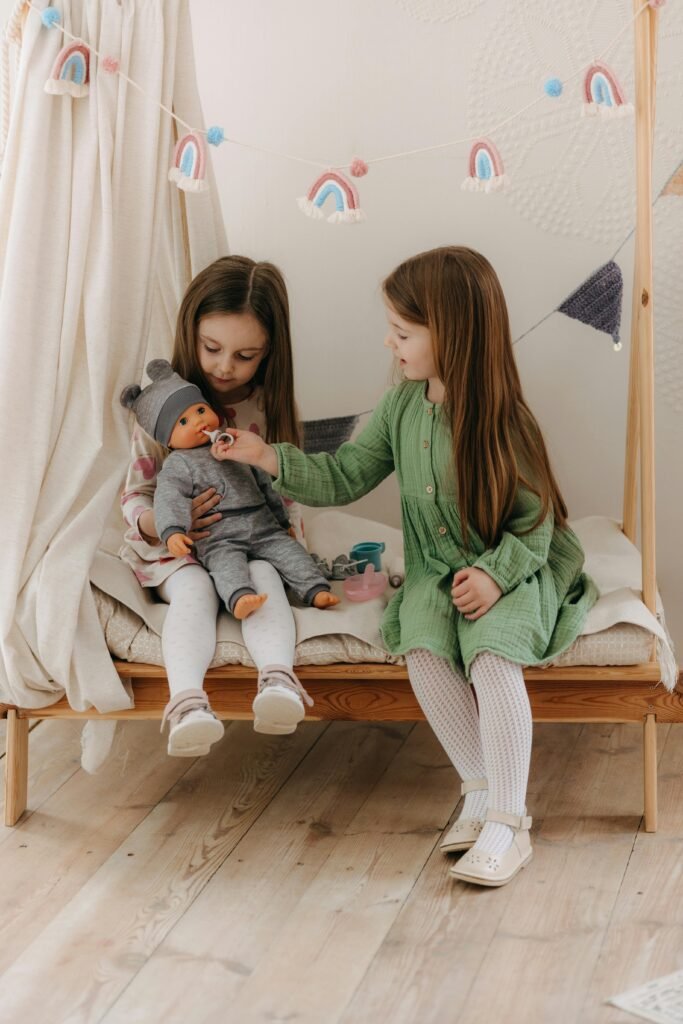 Two young girls enjoy playtime with a doll in a cozy indoor space, showcasing warmth and togetherness.